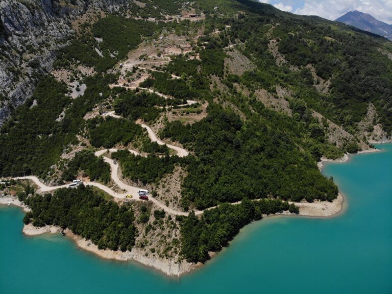 Stunning aerial shot of a winding road near a turquoise lake in the Albanian mountains.